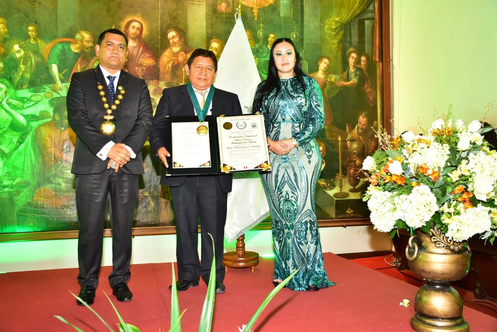 Tres personas durante una ceremonia mostrando documentos de reconocimiento.